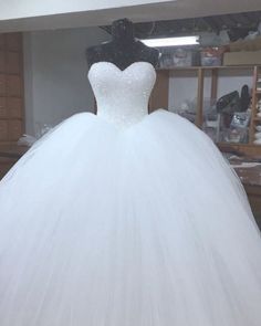 a white ball gown is on display in a room with shelves and other items behind it