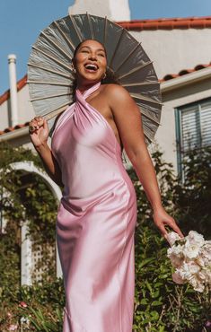 a woman in a pink dress holding an umbrella over her head and smiling at the camera