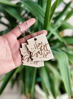 a hand holding a wooden keychain with the words home sweet in it on it