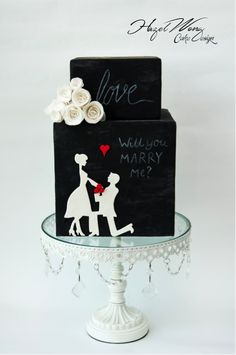 a black and white cake with a couple holding hands on top of it, which reads love will you marry me?