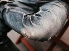 a person sitting on a chair with their feet in his jeans and holding onto the seat