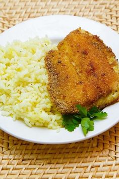 a white plate topped with rice and fried chicken next to green garnishes