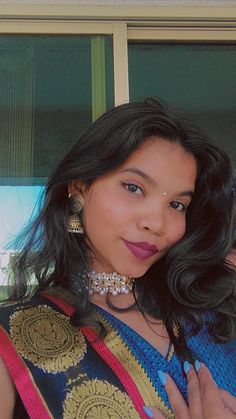 a woman with dark hair wearing a colorful top and earrings, posing for the camera