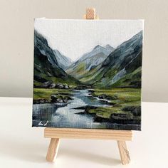 a small easel with a painting on it and mountains in the backgroud