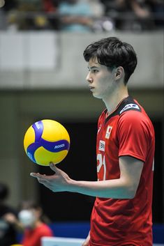 a young man holding a yellow and blue ball in his hand while wearing a red shirt