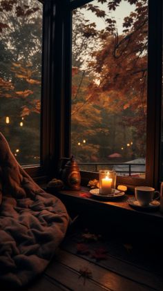 candles are lit in front of a window with autumn leaves on the ground and trees outside