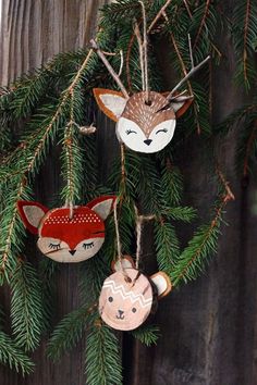 three ornaments hanging from a pine tree on a wooden fence, with the faces of two foxes and a fox