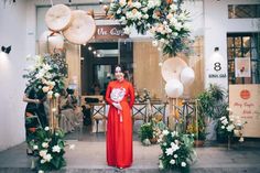 a woman standing in front of a flower shop with flowers on the windows and decorations around her