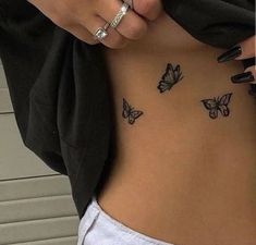 a woman's stomach with butterflies tattooed on the side and her hand holding onto it