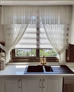 a kitchen with a sink, dishwasher and window covered in sheer curtaines