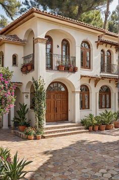 a large white house with lots of windows and plants on the front porch, surrounded by greenery