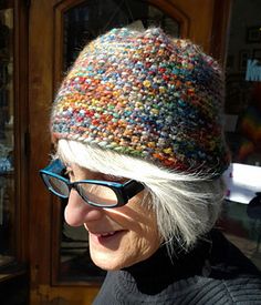 an older woman wearing glasses and a multicolored knitted hat looks at the camera