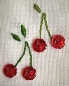 three red buttons with green stems on a white cloth covered tablecloth, one has been stitched to the side