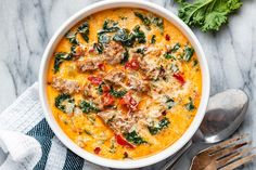 a bowl of soup with meat and spinach on the side next to silverware