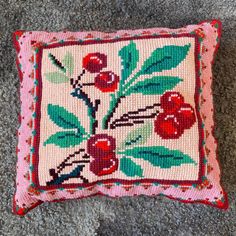 an embroidered pillow with cherries on it sitting on the floor next to a gray carpet