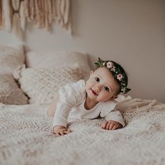 a baby laying on top of a bed wearing a flower crown