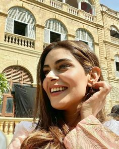 a woman is smiling while talking on her cell phone in front of an old building