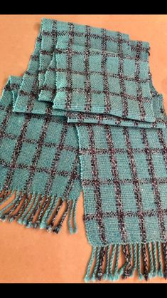 two pieces of blue and black plaid fabric with tassels on the ends, laying on a table