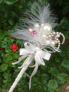 a white flower with pearls and feathers on it's headband is sitting in front of some green leaves