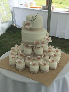 a wedding cake with white frosting and pink flowers on the top is surrounded by small cupcakes