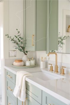 a bathroom with green cabinets and gold faucets on the counter top, along with a white towel draped over the sink