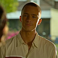 a man standing in front of a woman talking to each other while wearing a tan shirt