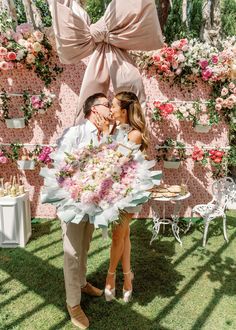 a man and woman standing next to each other in front of a wall covered with flowers