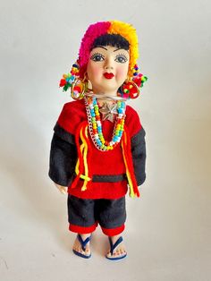 a small doll with colorful hair and beads on it's head, standing in front of a white background