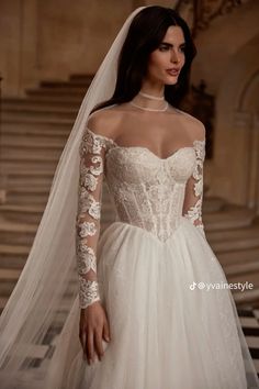 a woman wearing a wedding dress with long sleeves and a veil on her head is standing in front of stairs