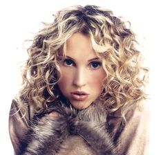 a woman with long curly hair wearing a fur collared coat and posing for the camera