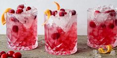 three glasses filled with ice and cranberries on top of a wooden table next to orange peels