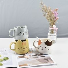 two coffee mugs sitting on top of a table next to a vase with flowers