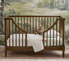 a teddy bear sitting on top of a crib in front of a wall mural