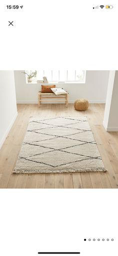 an image of a living room with white walls and wood flooring, including a large rug