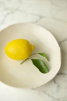 a lemon sitting on top of a white plate with a green leaf next to it