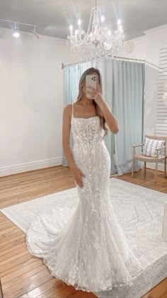 a woman taking a selfie in a wedding dress with a chandelier hanging from the ceiling