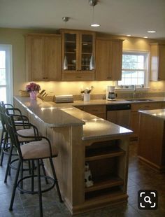 a large kitchen with an island and bar stools next to it, along with two windows