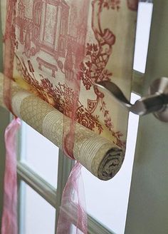 a roll of toilet paper is hanging on the wall next to a window with pink ribbon