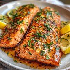 two salmon fillets on a plate with lemon wedges