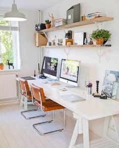 a white desk topped with two computer monitors next to a wall mounted shelf filled with books