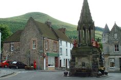 an old clock tower in the middle of a small town with mountains in the background