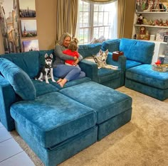 a woman sitting on top of a blue couch with two dogs in front of her