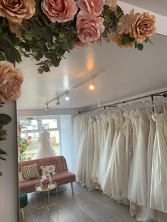 a room filled with lots of white dresses and flowers hanging from the ceiling next to a couch