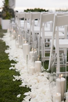 rows of white chairs lined up with flowers and candles on the grass in front of them