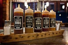 six bottles of bbq sauce sit on a wooden tray in front of the bar