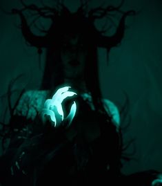 a woman holding a glowing object in her hands with dark hair and horns on her head