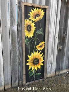 a painting of sunflowers painted on a wooden frame in front of a fence