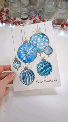 a hand holding up a christmas card with ornaments on it