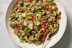 a white bowl filled with rice and vegetables on top of a marble table next to a spoon