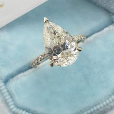 an engagement ring with a pear shaped diamond on top in a blue velvet box,